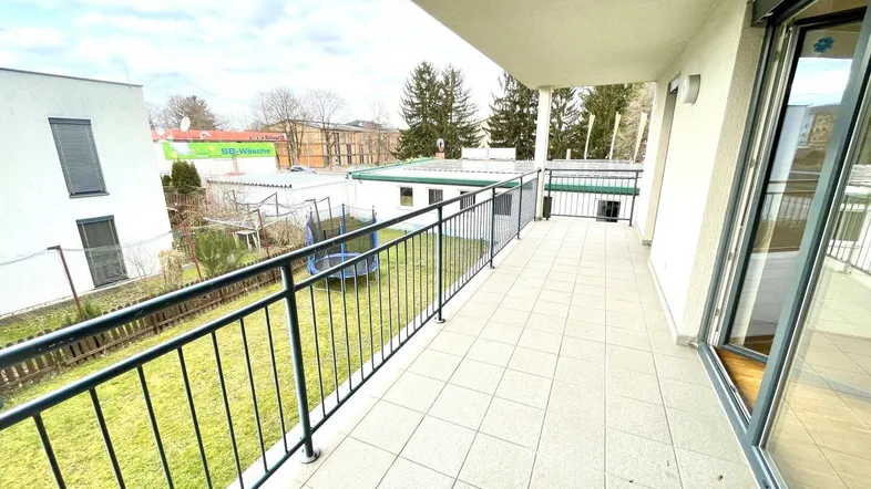 Geräumiger Balkon mit Fliesenboden und Blick auf den Gartenbereich und die Umgebung.