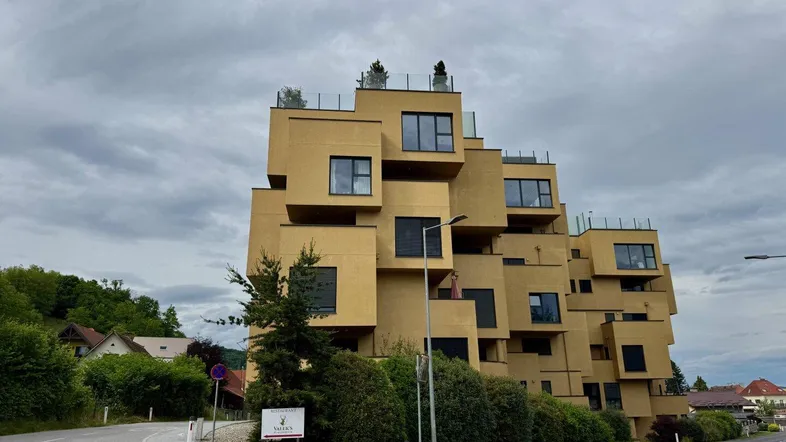 Modernes Gebäude mit gestufter Architektur und vielen Fenstern unter bewölktem Himmel.