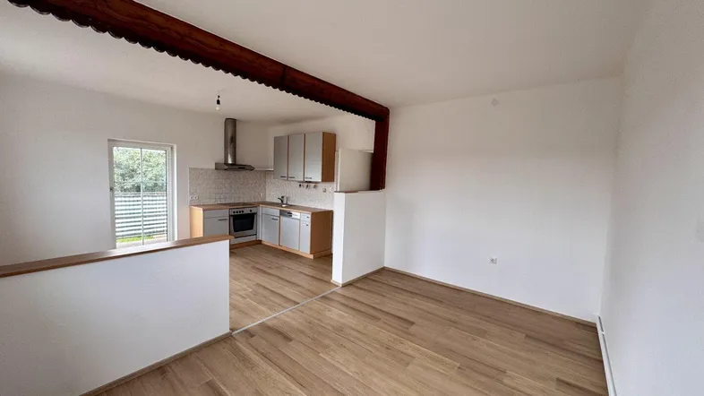 Offener Wohnbereich mit integrierter Küche, Holzbalken und hellem Laminatboden.