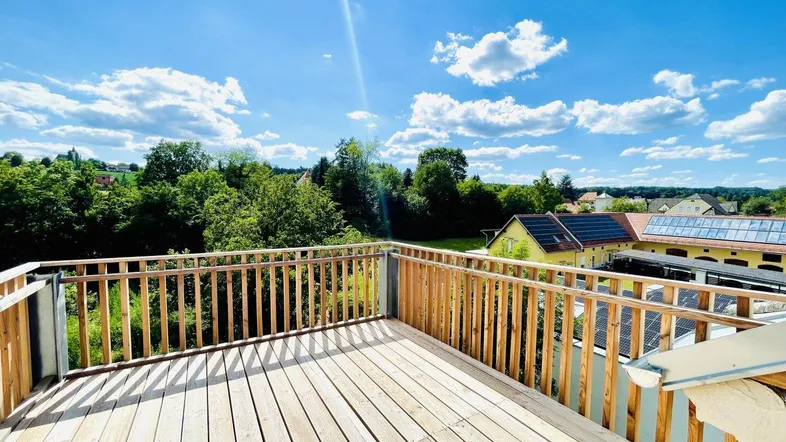 Große Holzterrasse mit weitem Blick ins Grüne und auf die umliegende Landschaft unter blauem Himmel.