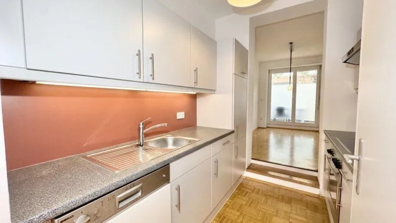 Helle Küche mit Spülmaschine, Spüle und Blick in den angrenzenden Wohnbereich.