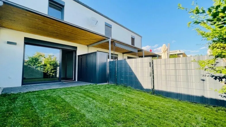 Heller Gartenbereich hinter dem Reihenhaus mit Rasenfläche und Zugang zur Terrasse.