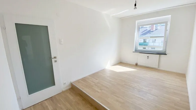 Helles Zimmer mit Holzboden und erhöhter Plattform, ideal als Schlaf- oder Arbeitsbereich.