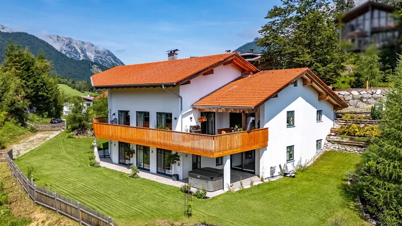 Großzügiges Haus mit Balkon, Garten und Bergblick unter blauem Himmel.