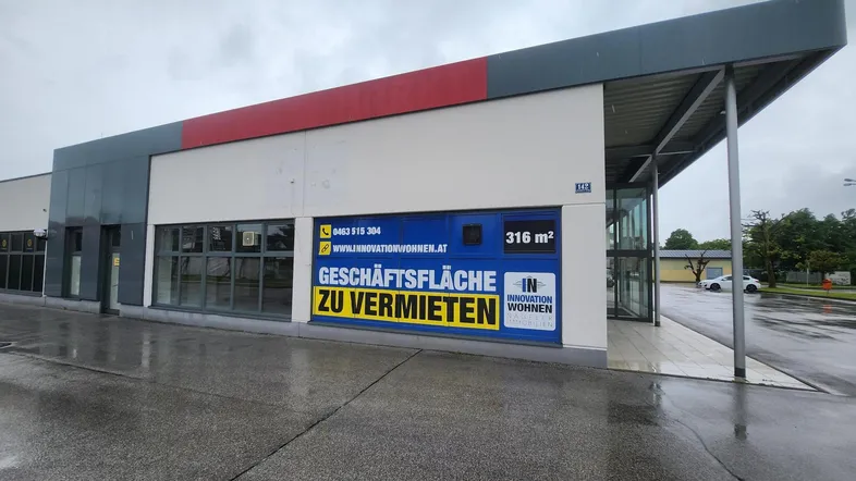 Außenansicht eines modernen Geschäftsgebäudes mit großen Fenstern und einer Werbeplane zur Vermietung.