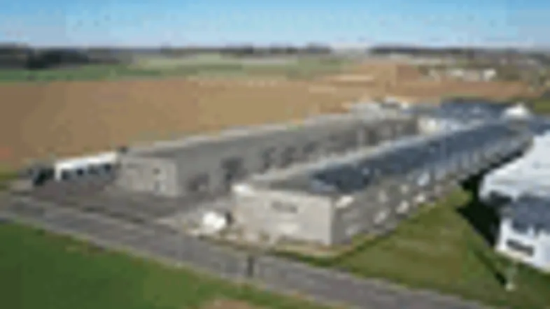 Luftaufnahme von zwei großen Industriegebäuden mit Solarpaneelen auf den Dächern, umgeben von Feldern.