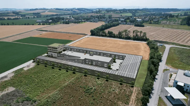 Luftaufnahme eines modernen Gewerbekomplexes mit Photovoltaikanlage, umgeben von ländlicher Landschaft.