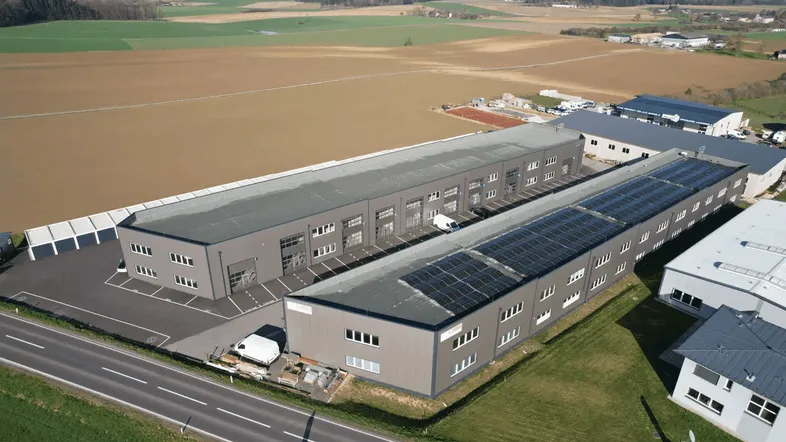 Luftaufnahme eines modernen Industriegebäudekomplexes mit Photovoltaikanlage und angrenzenden Feldern.