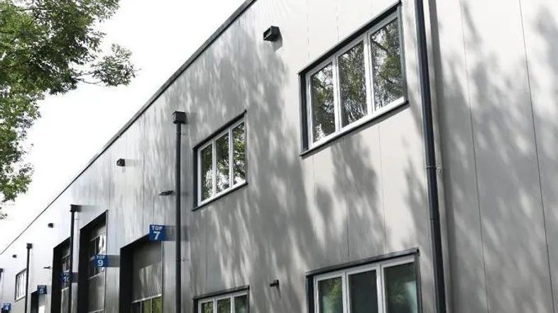 Moderne Gewerbeimmobilie mit grauer Fassade, großen Fenstern und Parkplätzen im Freien.