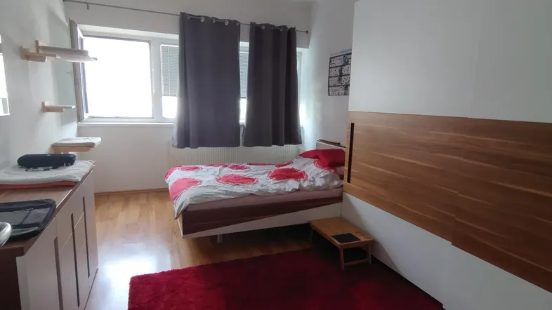 Helles Schlafzimmer mit Holzelementen, einem gemütlichen Bett und einem Fenster mit dunklen Vorhängen.