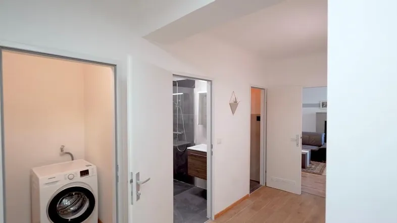 Heller Flur mit Zugang zu einem Hauswirtschaftsraum und einem modernen Badezimmer mit Dusche.