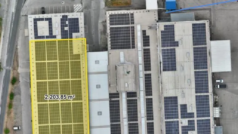 Luftaufnahme von Industriegebäuden mit umfangreichen Photovoltaikanlagen auf den Dächern und einem markierten Grundstück.