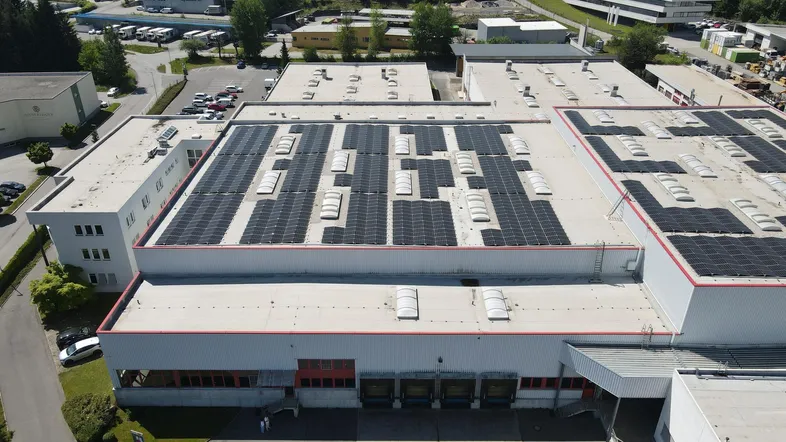 Luftaufnahme des Hauptgebäudes eines Industriekomplexes mit einer großen Photovoltaikanlage auf dem Dach.