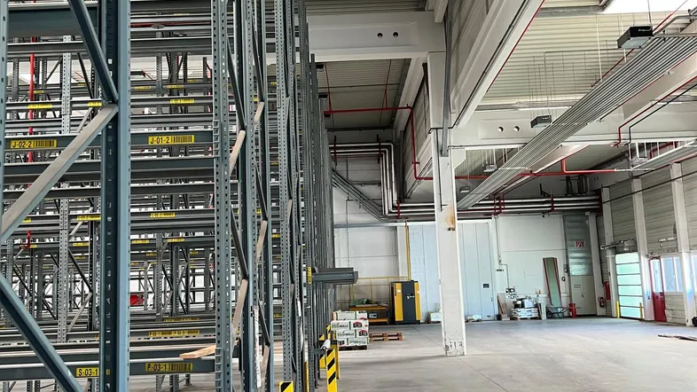 Große, leere Lagerhalle mit hohen Decken, Betonboden und robusten Metallregalen, bereit zur Nutzung.