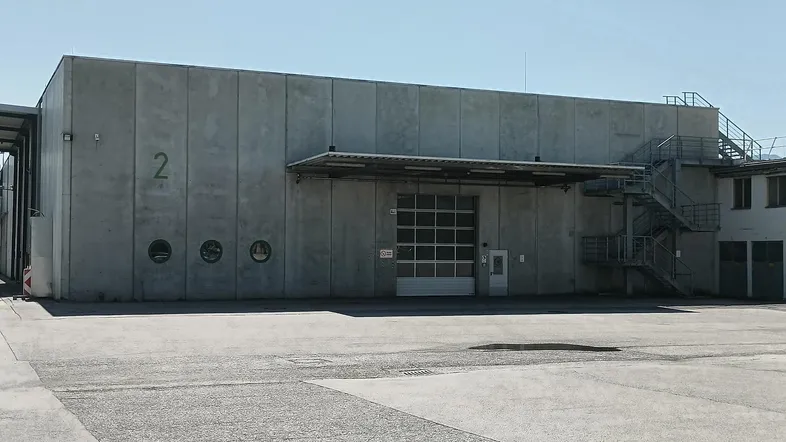 Industriegebäude mit Betonfassade, großem Rolltor und Außentreppe unter klarem Himmel.