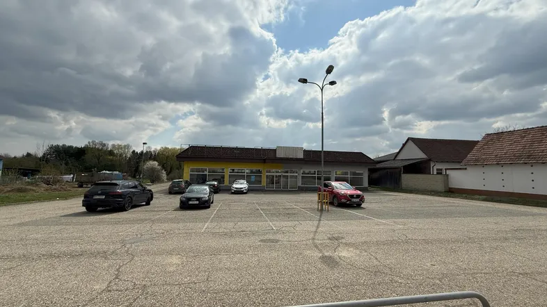 Außenansicht eines Gewerbegebäudes mit gelber Fassade und großem Parkplatz unter bewölktem Himmel.