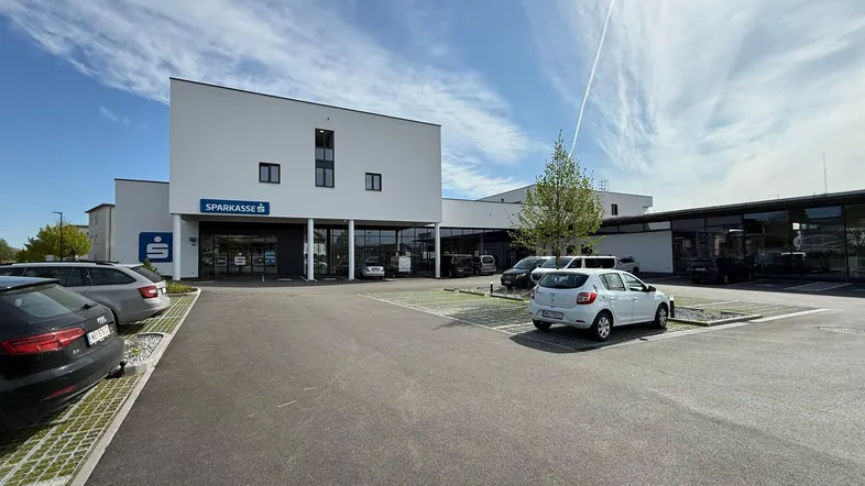 Modernes weißes Gebäude mit Sparkassen-Filiale und großem Parkplatz unter blauem Himmel.