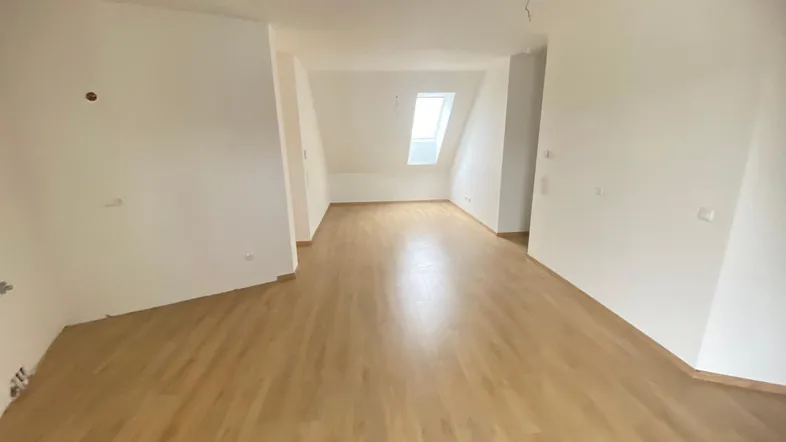 Helles Zimmer im Dachgeschoss mit Schrägdecken und neuem Laminatboden, ideal für Wohn- oder Schlafbereich.