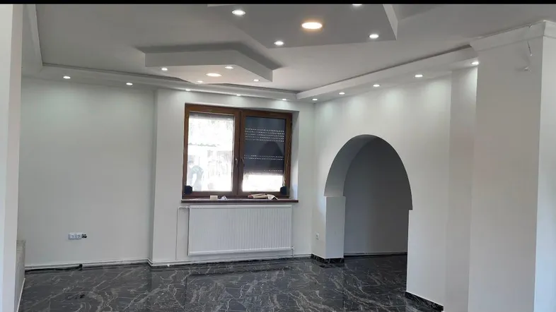 Heller Wohnraum mit modernem Deckenlicht, dunklem Marmorboden und elegantem Rundbogen.