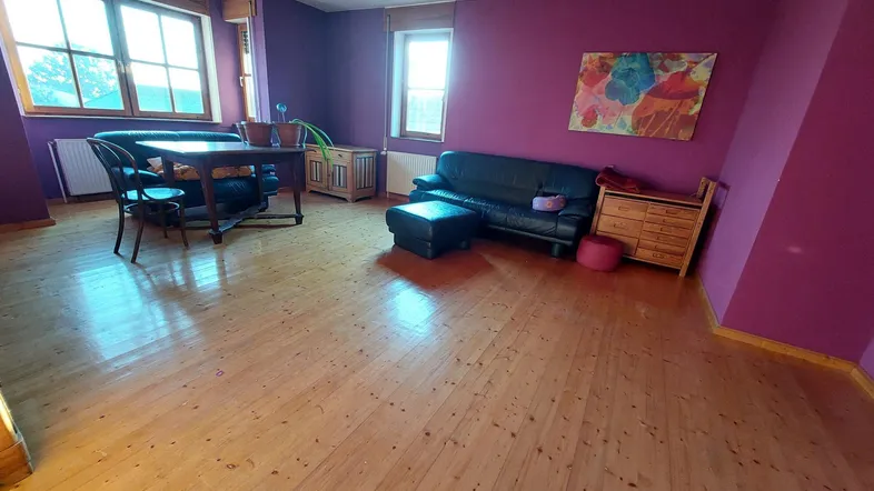Helles Wohnzimmer mit auffälligen violetten Wänden, Holzboden und gemütlicher Sitzecke.