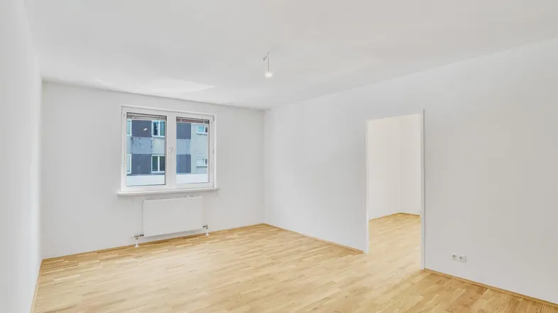 Geräumiges, helles Zimmer mit Parkettboden und großem Fenster, ideal als Wohn- oder Schlafzimmer.
