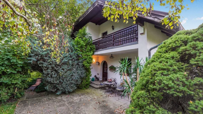 Gemütliche Terrasse vor dem Haus, umgeben von üppigem Grün und Bäumen.