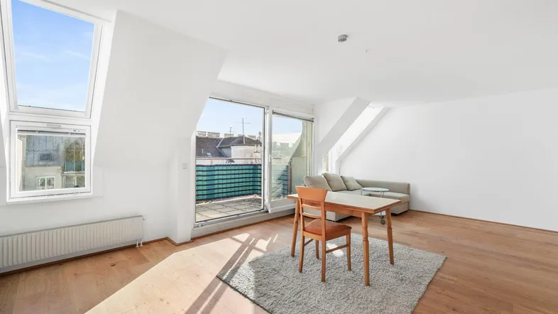 Helles Wohnzimmer im Dachgeschoss mit Holzboden, Dachfenstern und Zugang zum Balkon.