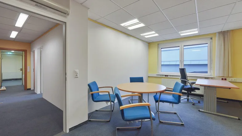 Geräumiges Büro mit Teppichboden, Besprechungstisch und Klimaanlage, ideal für Teamarbeit.