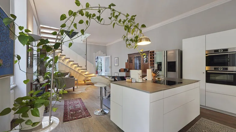 Moderner offener Wohnbereich mit integrierter Küche, Kochinsel und eleganter Treppe mit Beleuchtung.