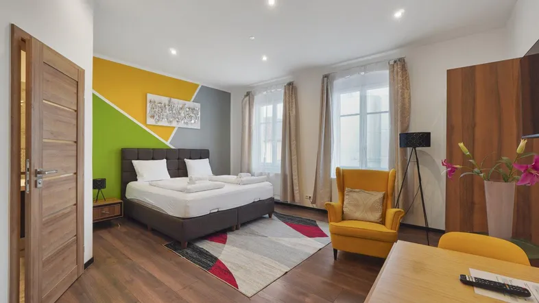 Geräumiges Schlafzimmer mit Doppelbett, farbiger Akzentwand und gemütlichem Sessel in hellem Ambiente.
