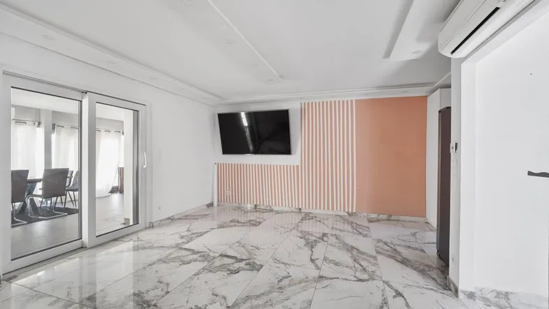 Geräumiges Wohnzimmer mit modernen Marmorfliesen, Klimaanlage und Zugang zu einem weiteren Raum.