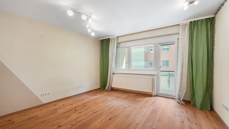 Wohnzimmer mit Holzboden, großen Fenstern und grünen Vorhängen, die den Raum schmücken.