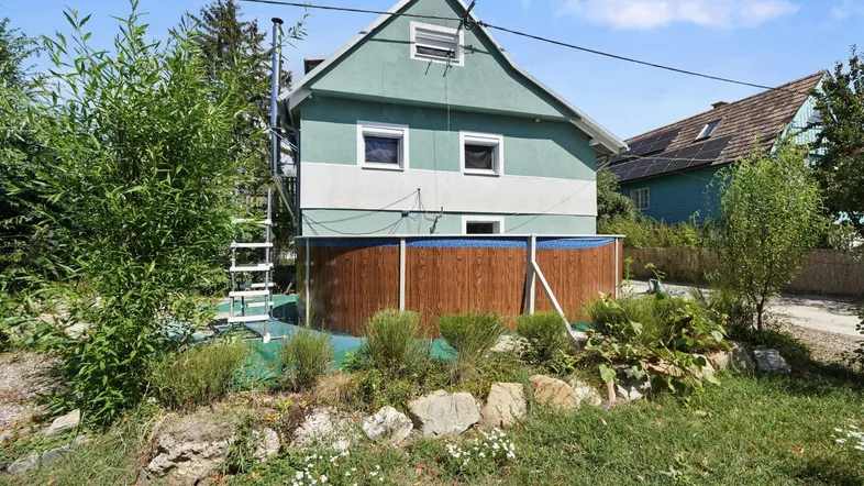 Rückansicht des Hauses mit einem oberirdischen Pool im Gartenbereich und viel Grün.