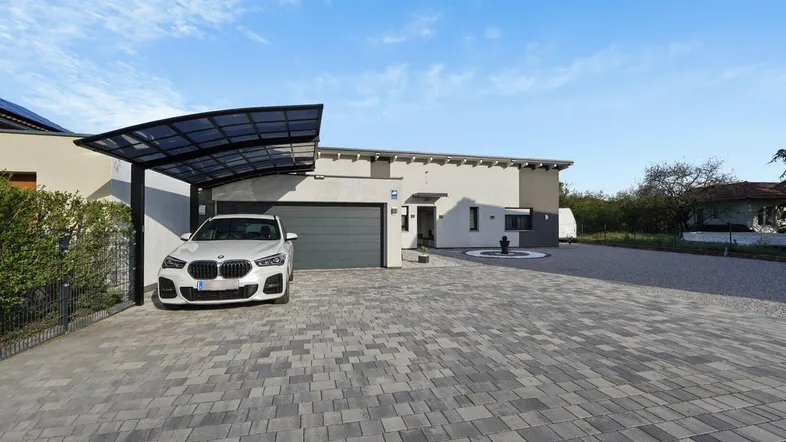 Modernes Einfamilienhaus mit Carport, gepflasterter Auffahrt und gepflegtem Vorgarten unter blauem Himmel.