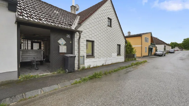 Hausfassade mit Satteldach und überdachtem Stellplatz an einer ruhigen Wohnstraße.