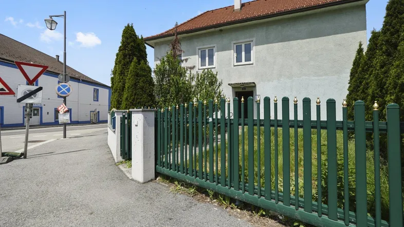 Vorderansicht eines Wohnhauses mit grünem Zaun und gepflegtem Vorgarten unter blauem Himmel.