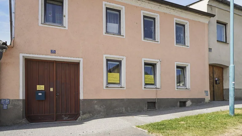Vorderansicht eines älteren Wohnhauses mit Putzfassade, mehreren Fenstern und einem Garagentor.