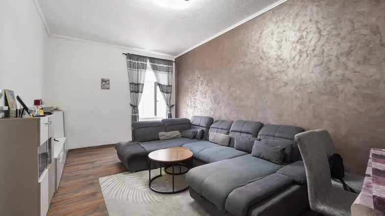 Gemütliches Wohnzimmer mit großem Ecksofa, Holzboden und einer Akzentwand in Braun.
