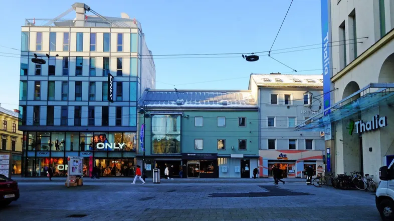 Blick auf eine belebte Einkaufsstraße mit modernen und traditionellen Gebäuden unter blauem Himmel.