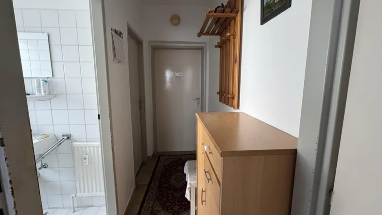 Heller Flur mit Holzmöbeln und Zugang zu einem gefliesten Badezimmer.