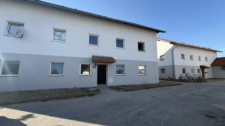 Mehrfamilienhaus mit weiß-grauer Fassade und Eingangsbereich unter blauem Himmel.