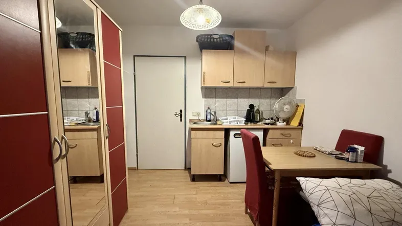 Kompakter Wohnbereich mit kleiner Küchenzeile, Esstisch und Spiegelschrank.