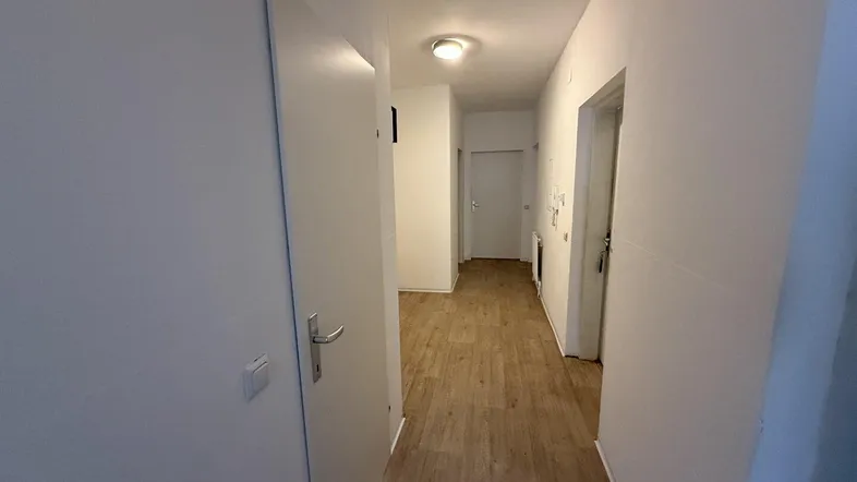 Heller Flur mit Laminatboden und weißen Wänden, der zu verschiedenen Räumen führt.