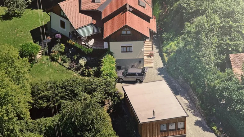 Luftaufnahme eines Einfamilienhauses mit Garten, Terrasse und separatem Nebengebäude in grüner Umgebung.