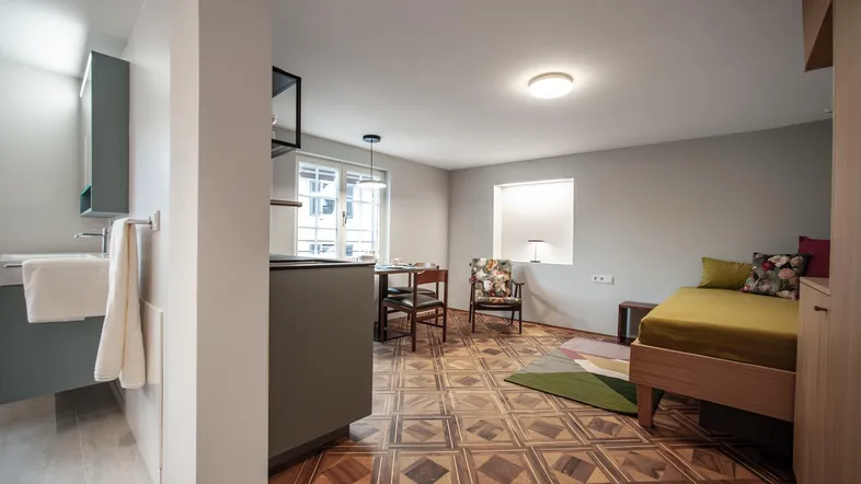 Helles Studio-Apartment mit gemustertem Parkettboden, Schlafbereich und Essplatz.