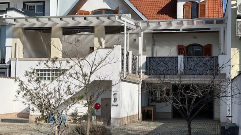Außenansicht eines Hauses mit gepflastertem Hof, Pergola und Balkonen im Obergeschoss.