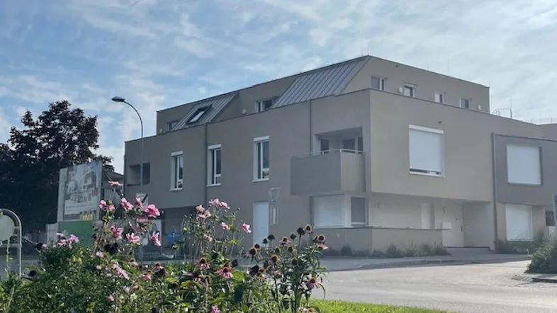 Modernes Mehrfamilienhaus mit grauer Fassade, Balkonen und gepflegter Bepflanzung im Vordergrund.