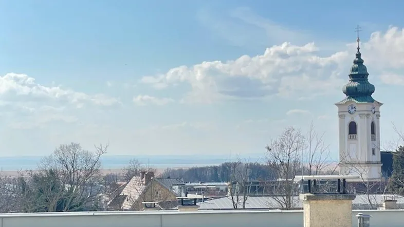 Panoramablick über Dächer und eine Kirche mit weitem Horizont unter blauem Himmel.
