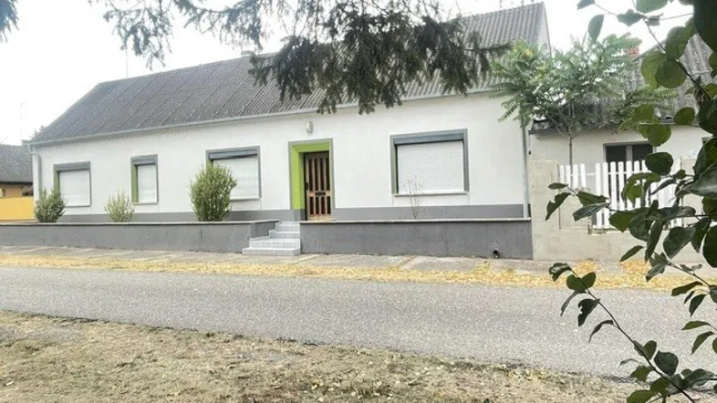 Weißes Einfamilienhaus mit grünem Eingangsbereich und grauen Fensterläden an einer ruhigen Straße.