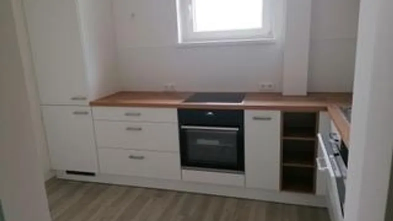 Helle Einbauküche mit weißen Schränken, Holzarbeitsplatte und integriertem Backofen.